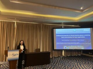 Marcela standing at the podium, with the slides of her presentation behind her.